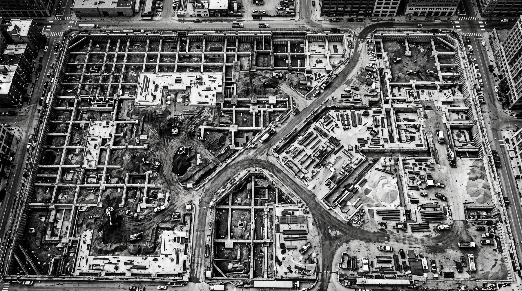 Aerial view of a large urban development site showing an excavated foundation grid and access roads.